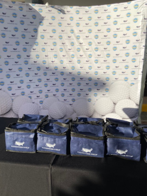 Table display with blue Nationwide Coils bags and a golf-themed backdrop.