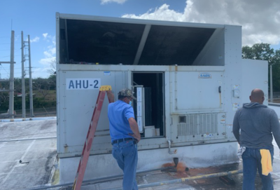 Two workers inspecting a rooftop HVAC unit labeled “AHU-2.”