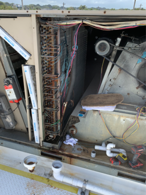 Opened rooftop HVAC unit showing internal coils, wiring, and components.
